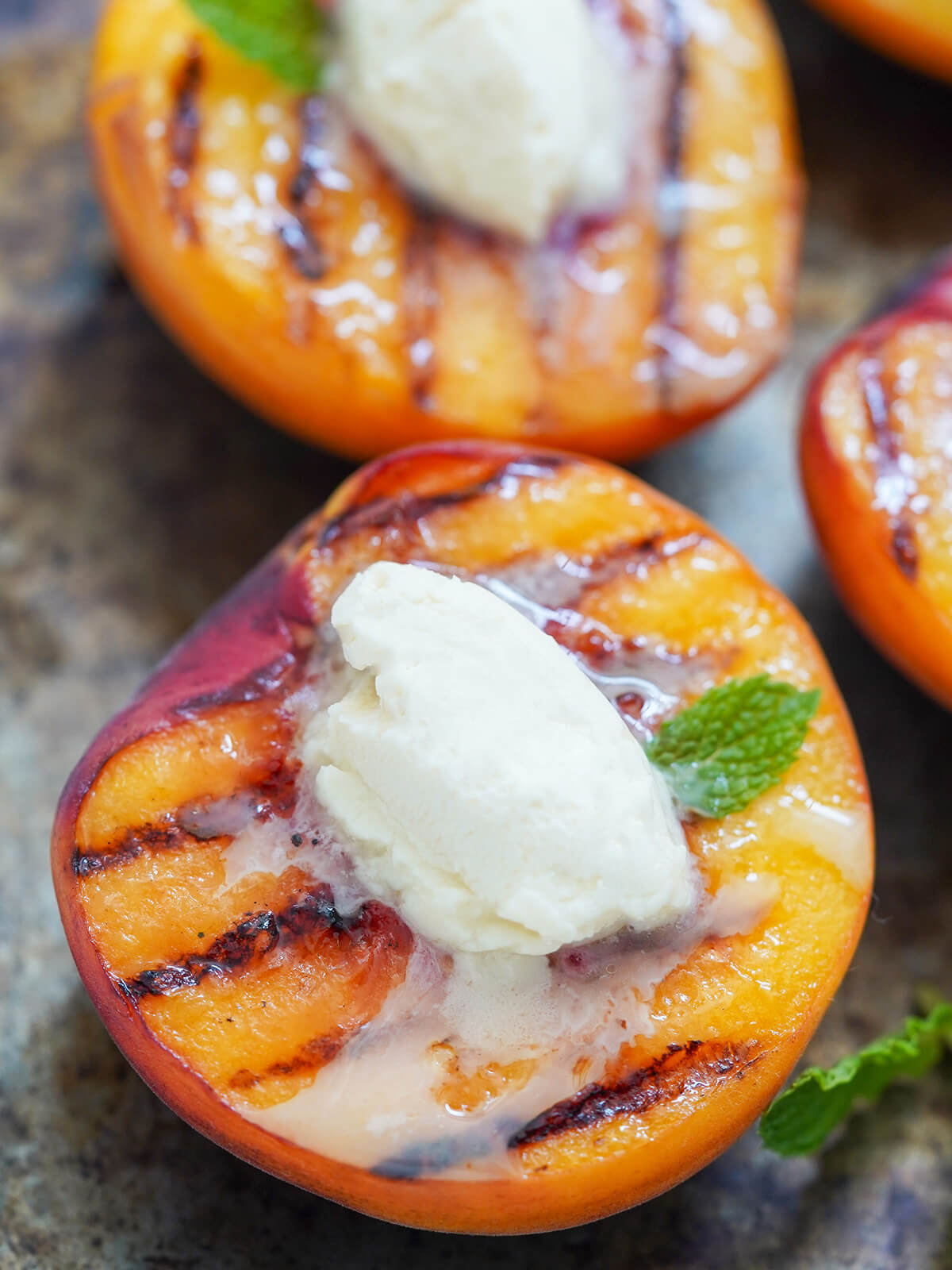 close up of a half grilled peach topped with mascarpone with another in part view behind.