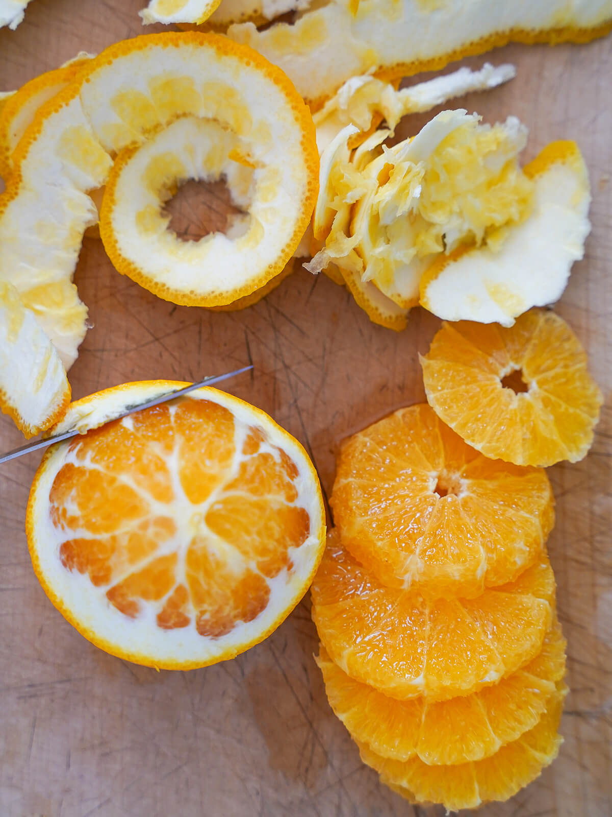 removing skin and pith from orange with another sliced to side.