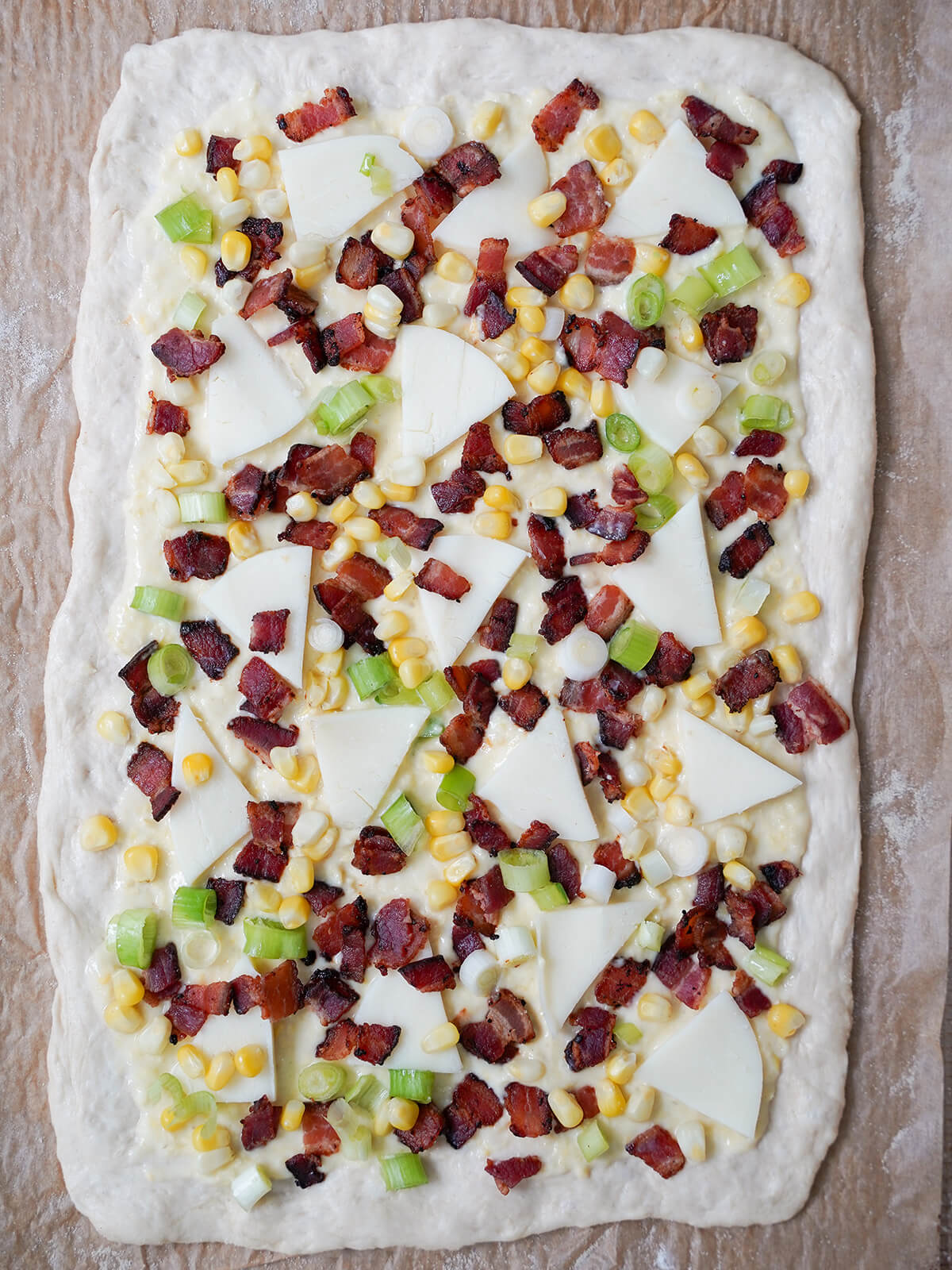 corn, bacon, cheese and scallion on top of creamy corn base on pizza dough before baking.