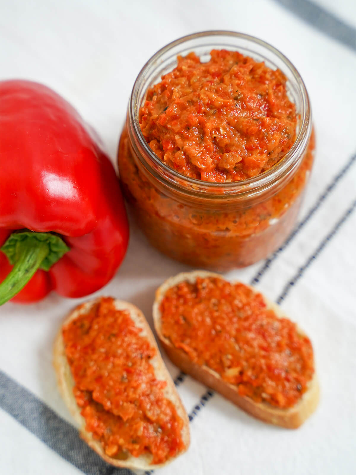 slightly overhead view of jar of ajvar red pepper spread overhead view of jar of ajvar red pepper spread with bread topped with it below.