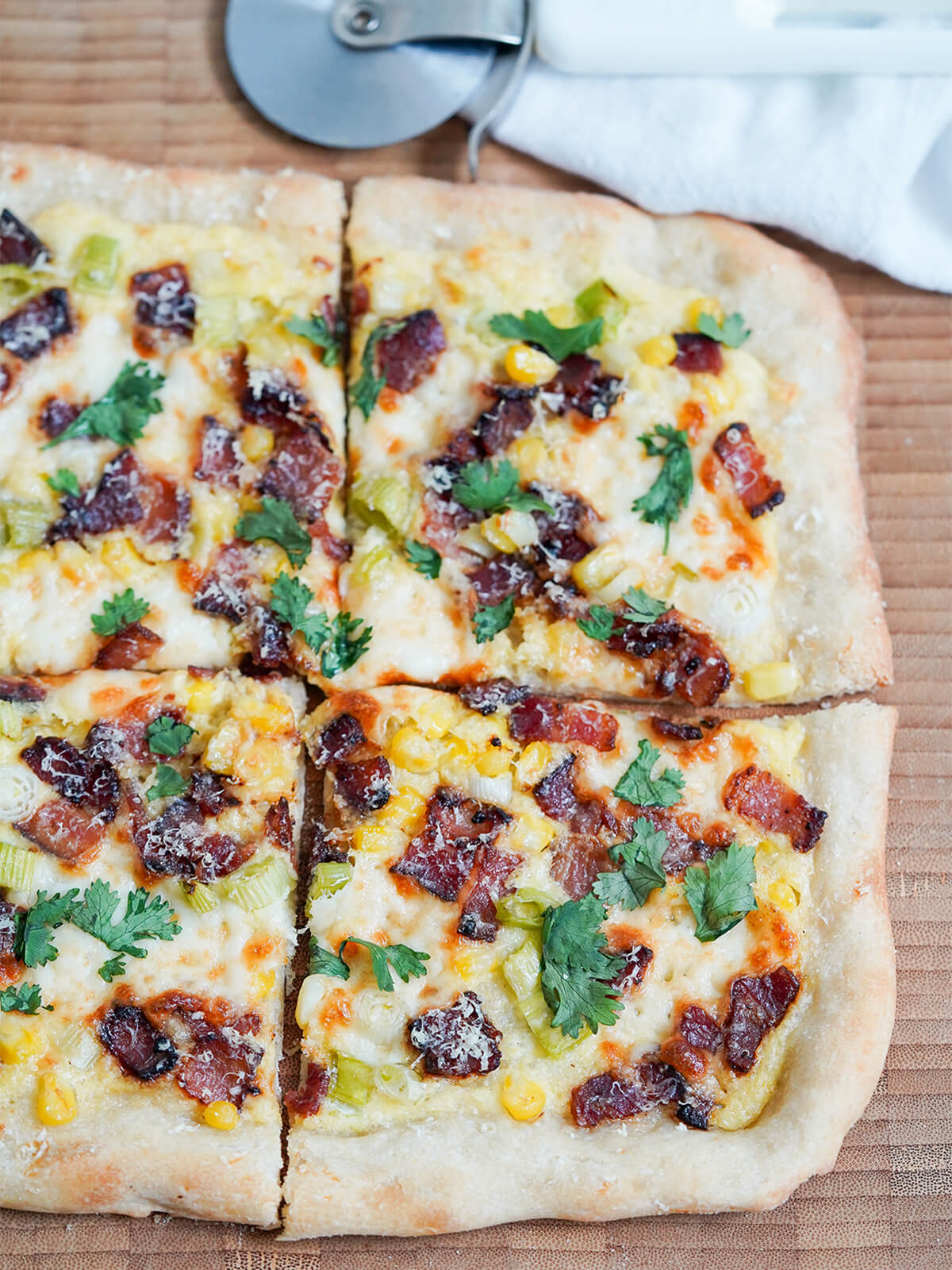 part of corn pizza with bacon cut into slices with pizza cutter behind.