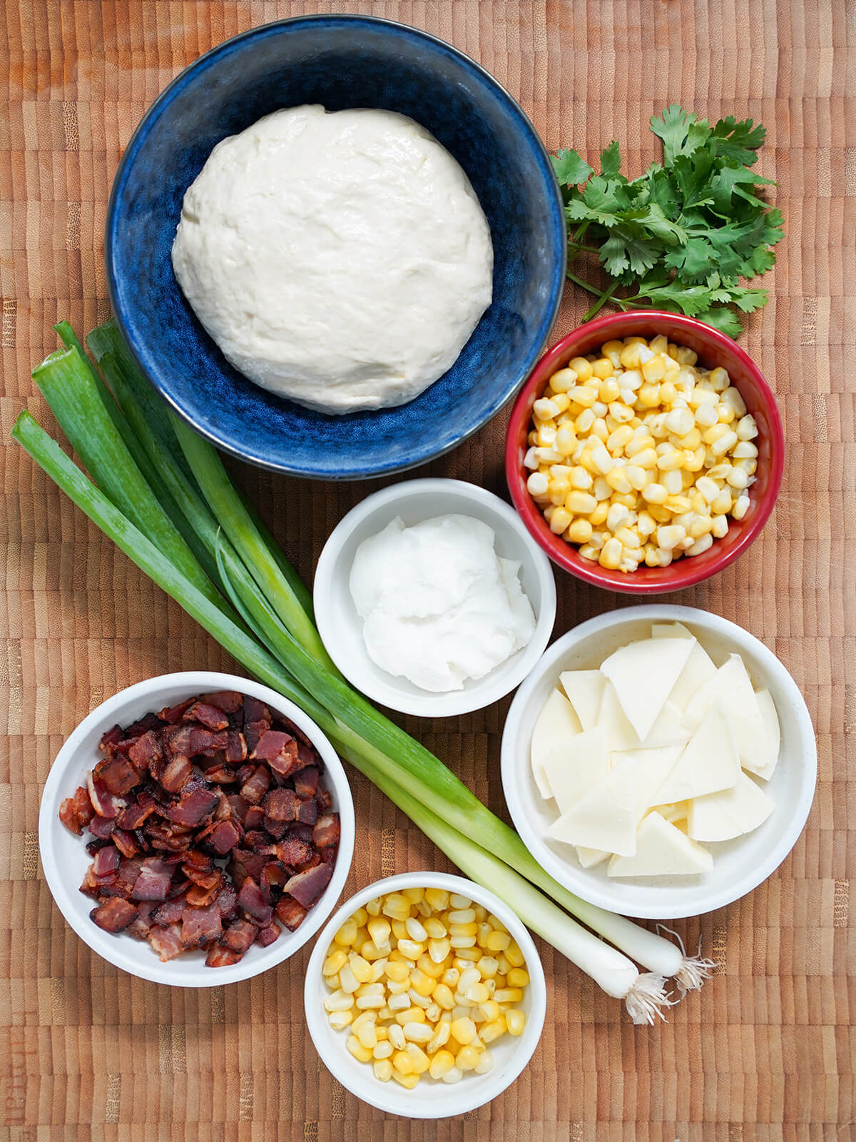bowl of pizza dough, with smaller bowls of corn, sliced mozzarella cheese, ricotta and bacon with scallions and some cilantro to side.