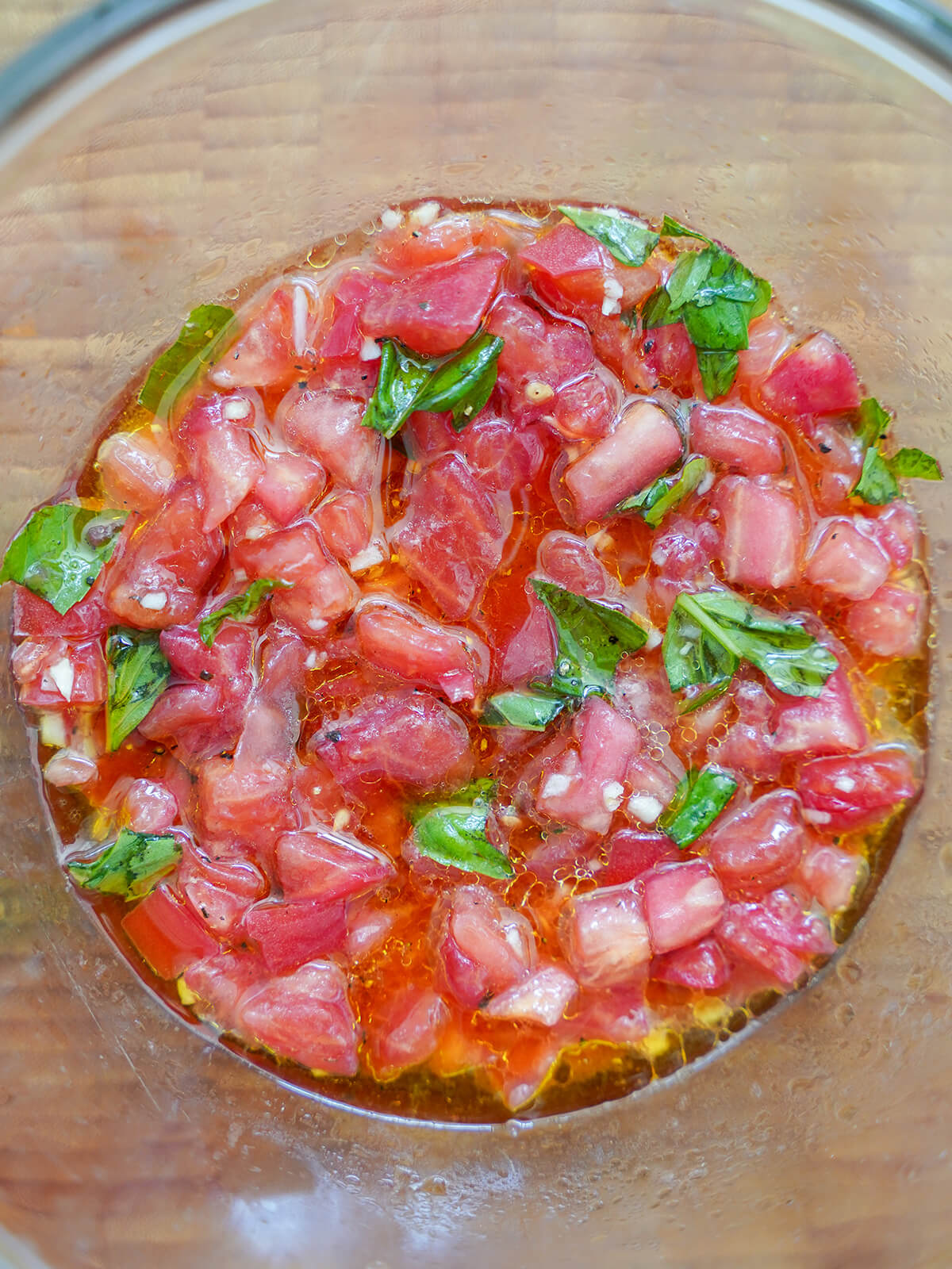 sauce mixture for spaghetti con pomodoro crudo, pasta with fresh tomatoes chopped tomatoes and basil in bowl with olive oil and specks of garlic.