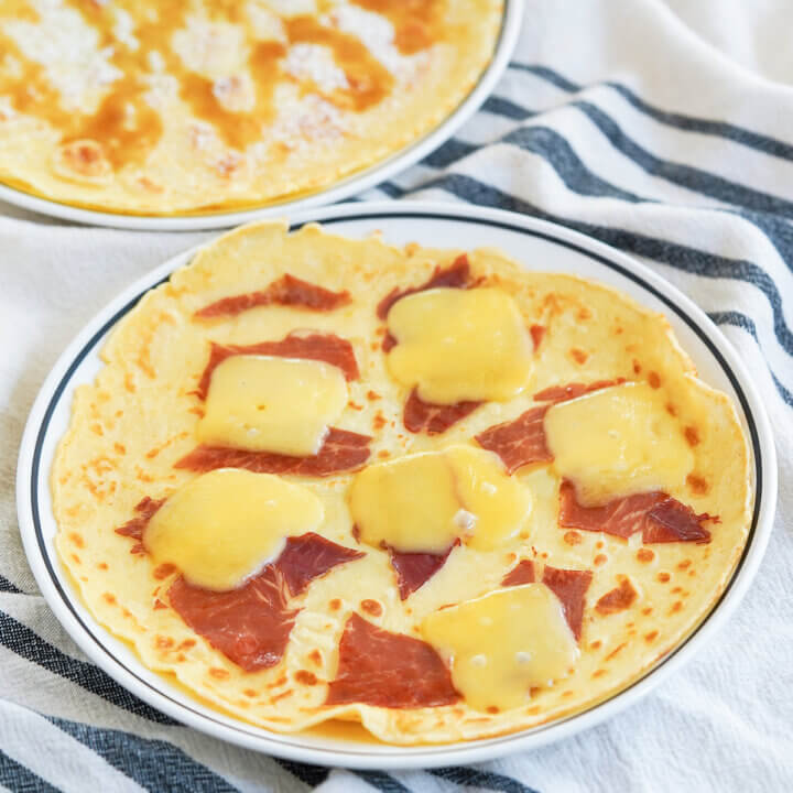 close view of plates of Pannekoeken Dutch pancakes, whole plate at front with ham and cheese and part behind with syrup on top.