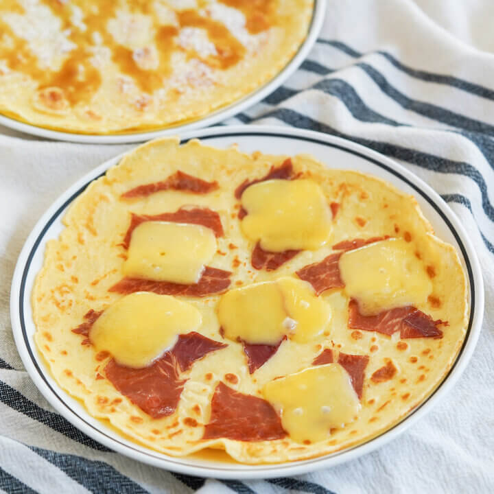 Dutch pancakes, pannekoeken, with one in front topped with ham and cheese.