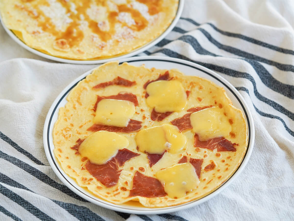clove view of plates of Pannekoeken Dutch pancakes, whole plate at front with ham and cheese and part behind with syrup on top.