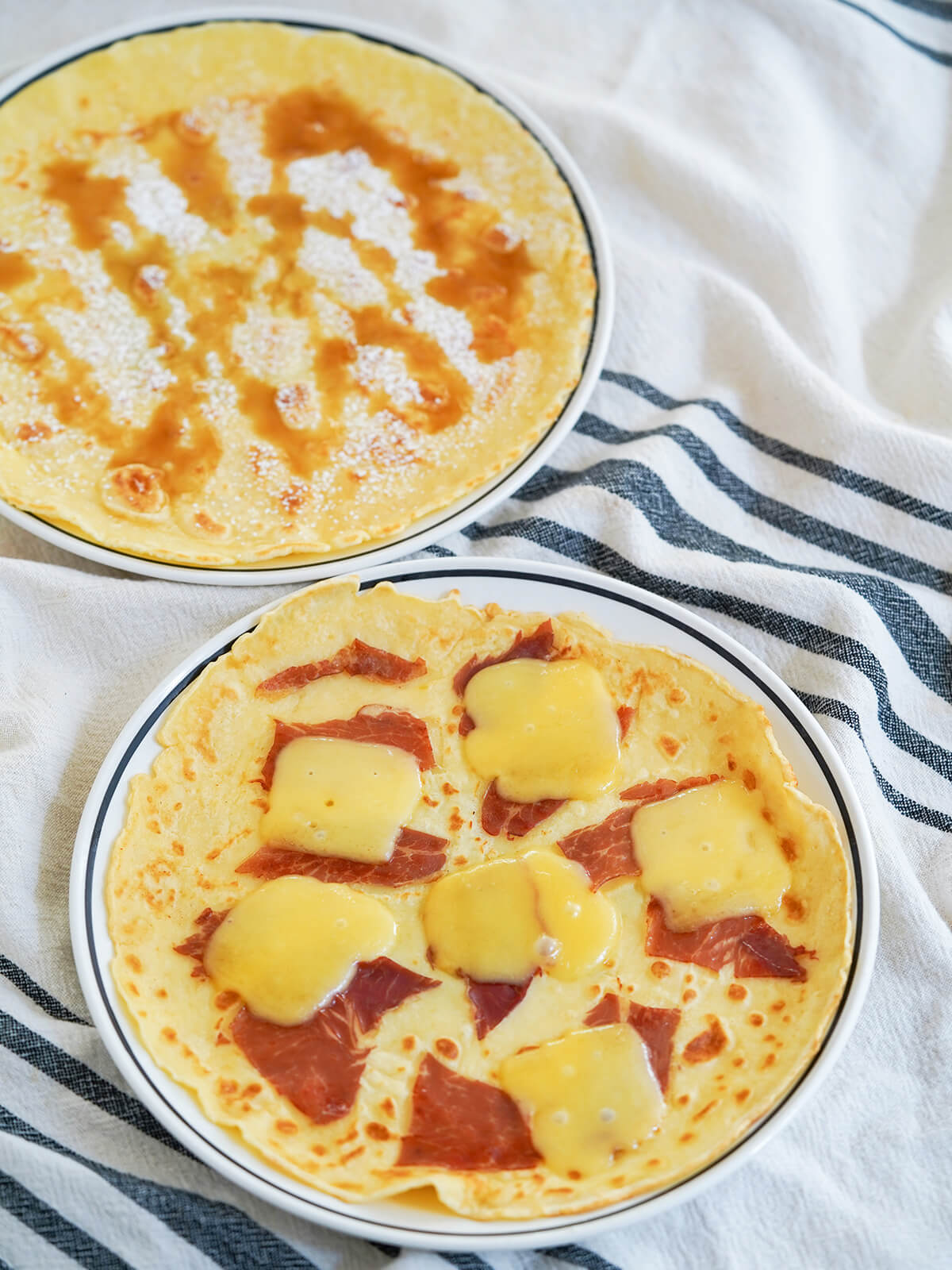 plates of Pannekoeken Dutch pancakes, front with ham and cheese and behind with syrup and sugar.