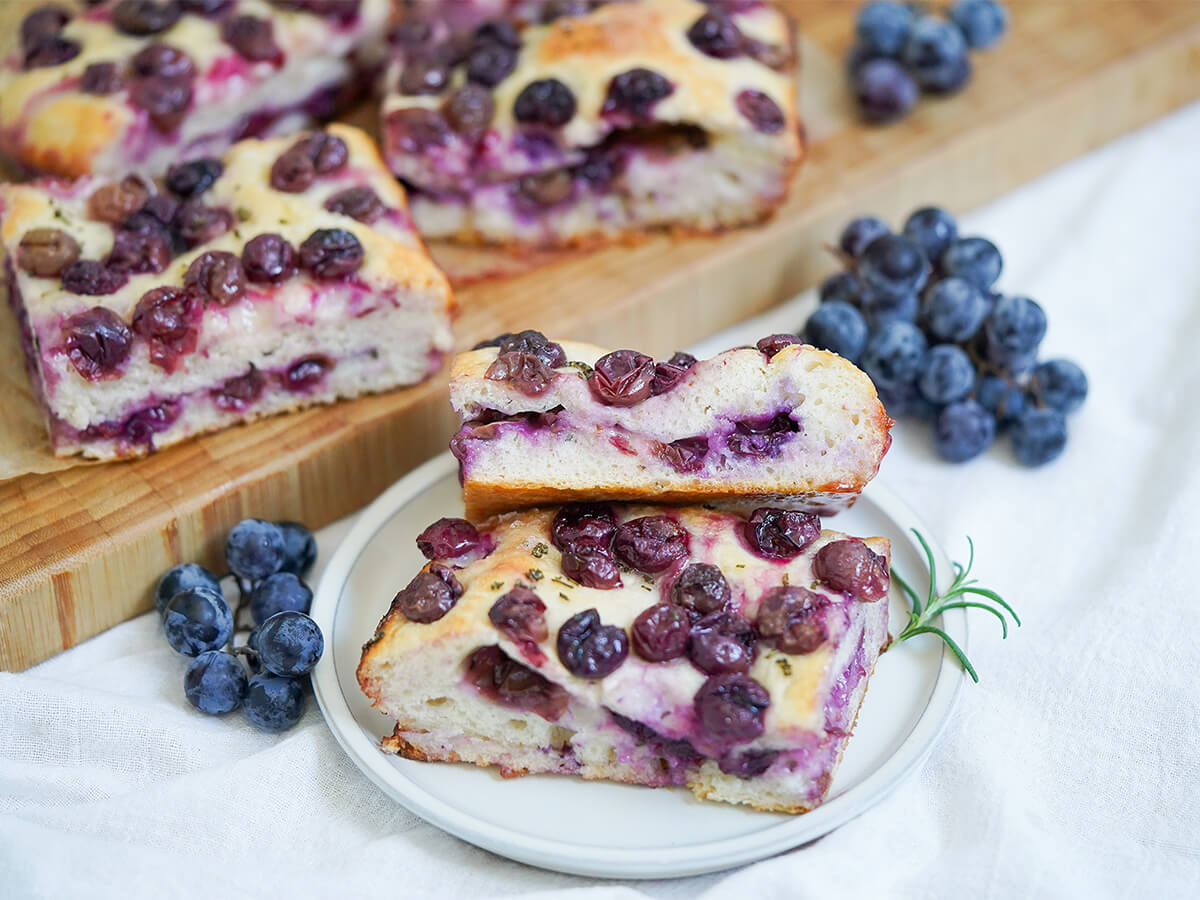 slices of Schiacciata all&rsquo;uva grape focaccia on plate with grapes wither side and more slices on board behind.