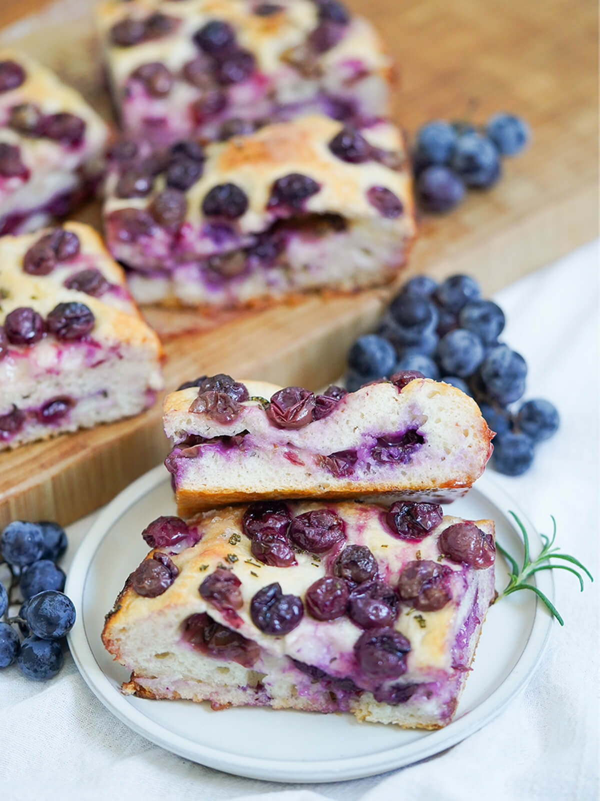 slices of Schiacciata all&rsquo;uva grape focaccia on plate with grapes and more slices on board behind.