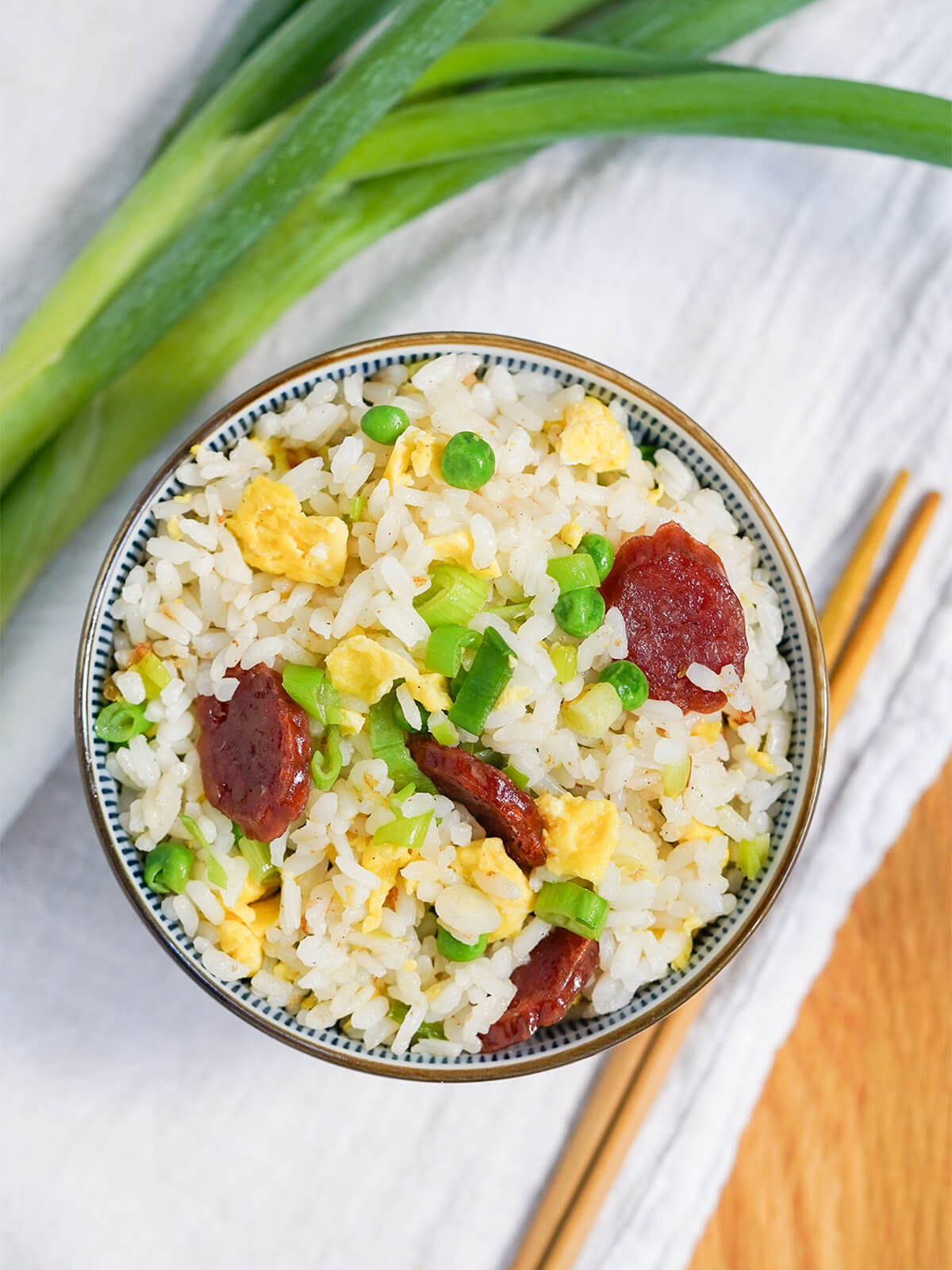 overhead view of bowl of Taiwanese fried rice overhead view of bowl of Taiwanese fried rice with chopsticks below bowl and scallion stems to side.