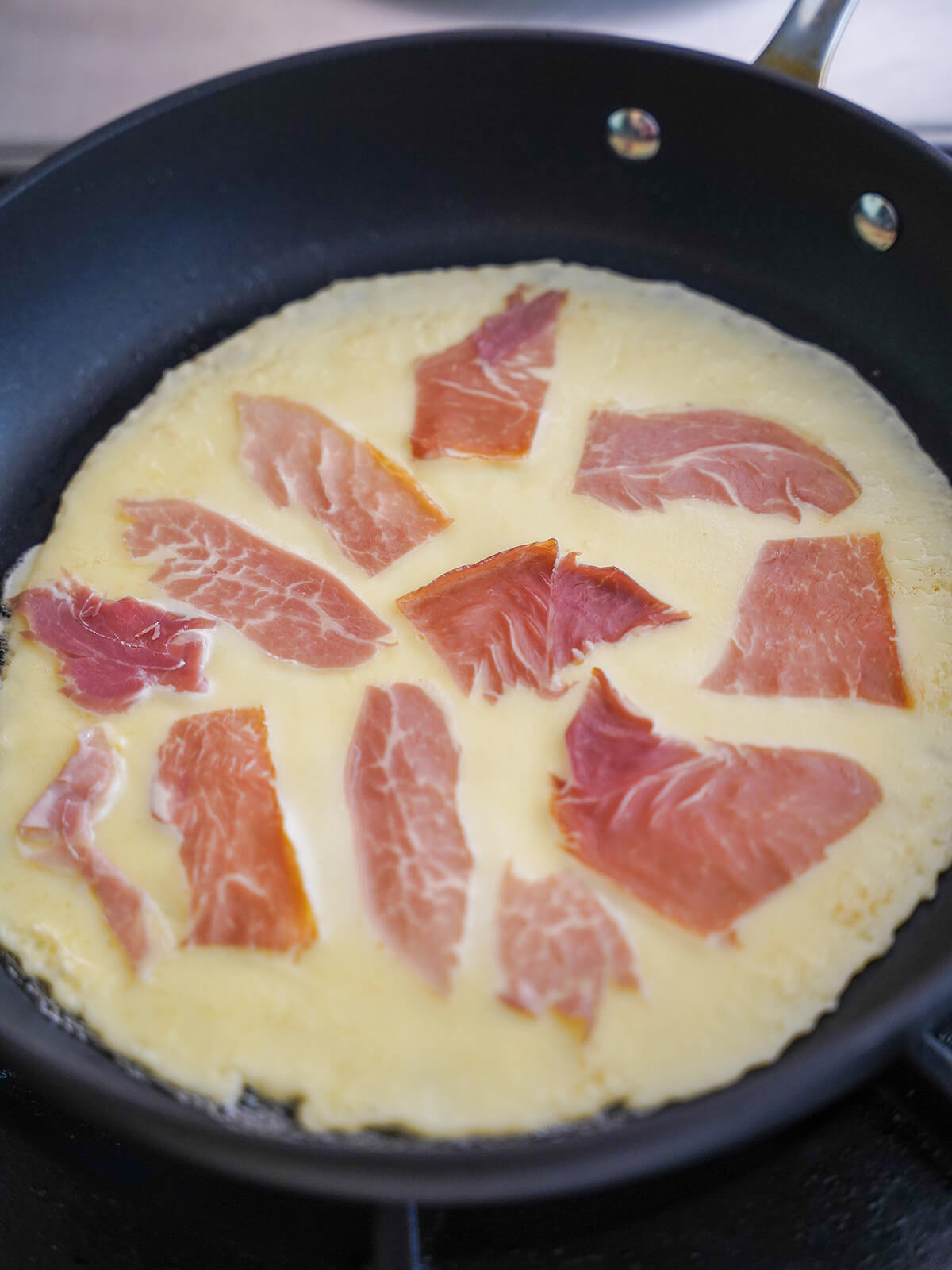 pieces of speck on top of part cooked pancake.