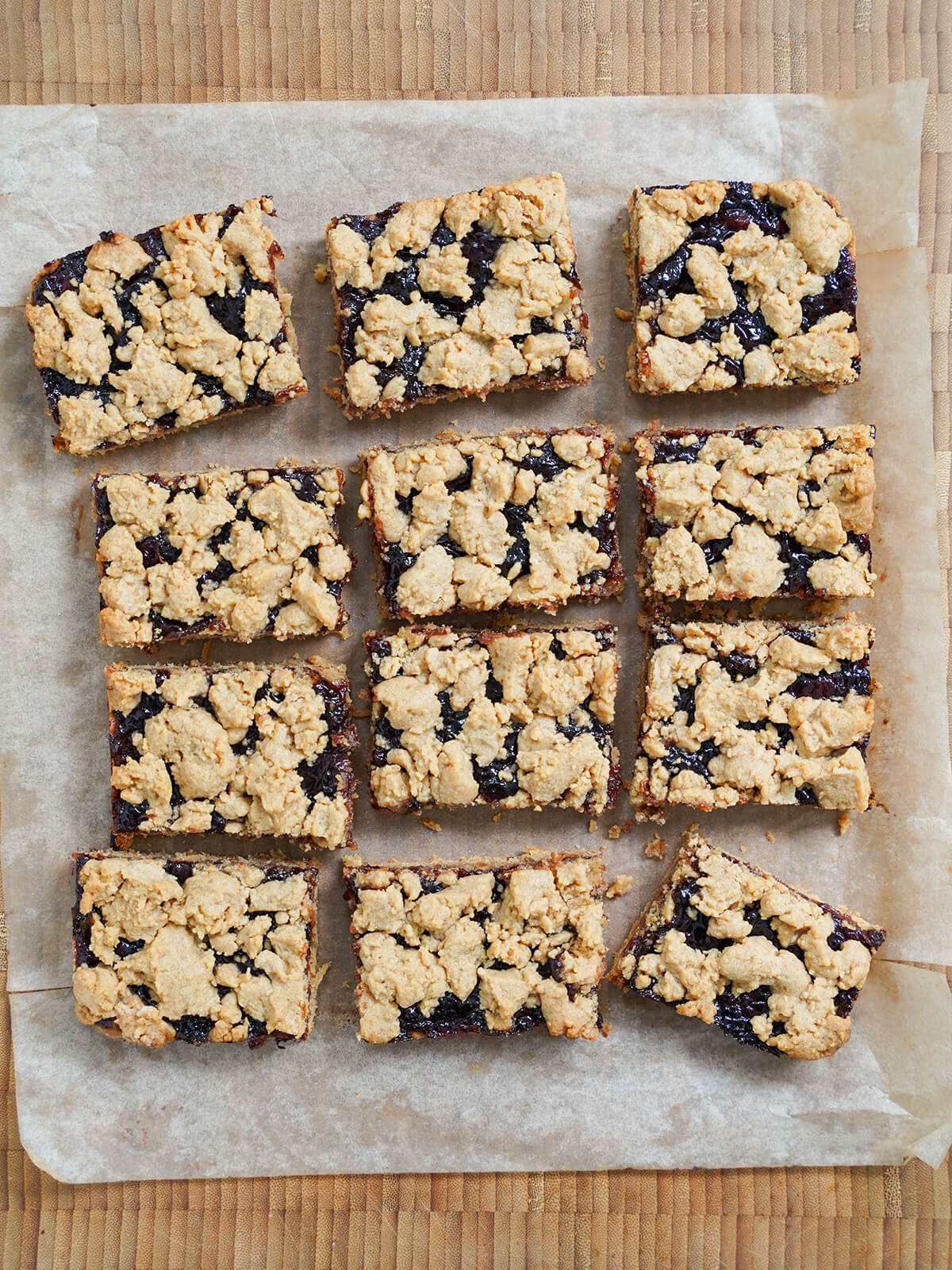 cut up slices of peanut butter and jelly bars on parchment on top of wooden board.