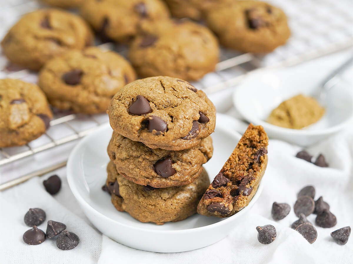 hojicha chocolate chip cookies stack of hojicha chocolate chip cookies on small plate with more on cooling rack behind and chocolate chips either side.
