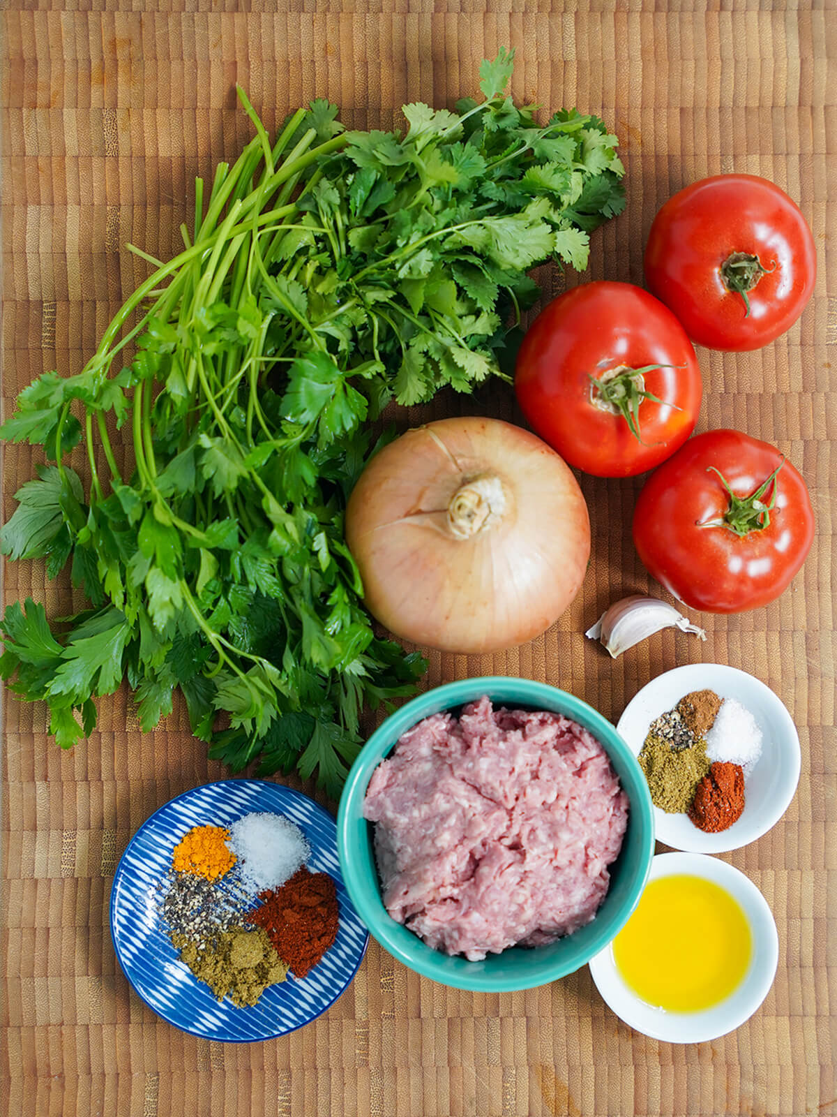 bunches of parsley and cilantro, tomatoes, onion, dishes with ground meat and spices.