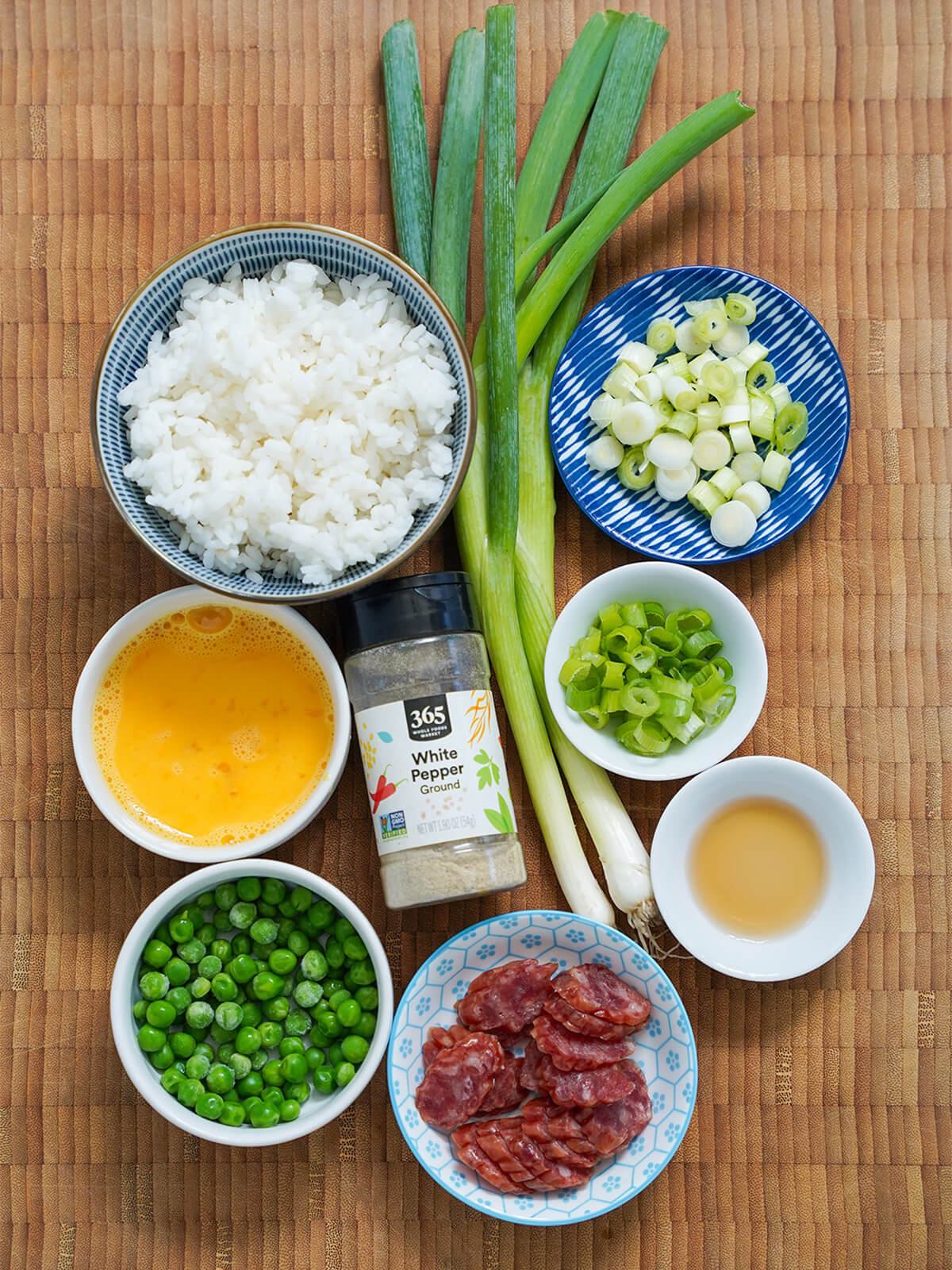 ingredients for Taiwanese fried rice bowls of rice, egg, peas, sliced sausage, scallions with jar white pepper in middle.