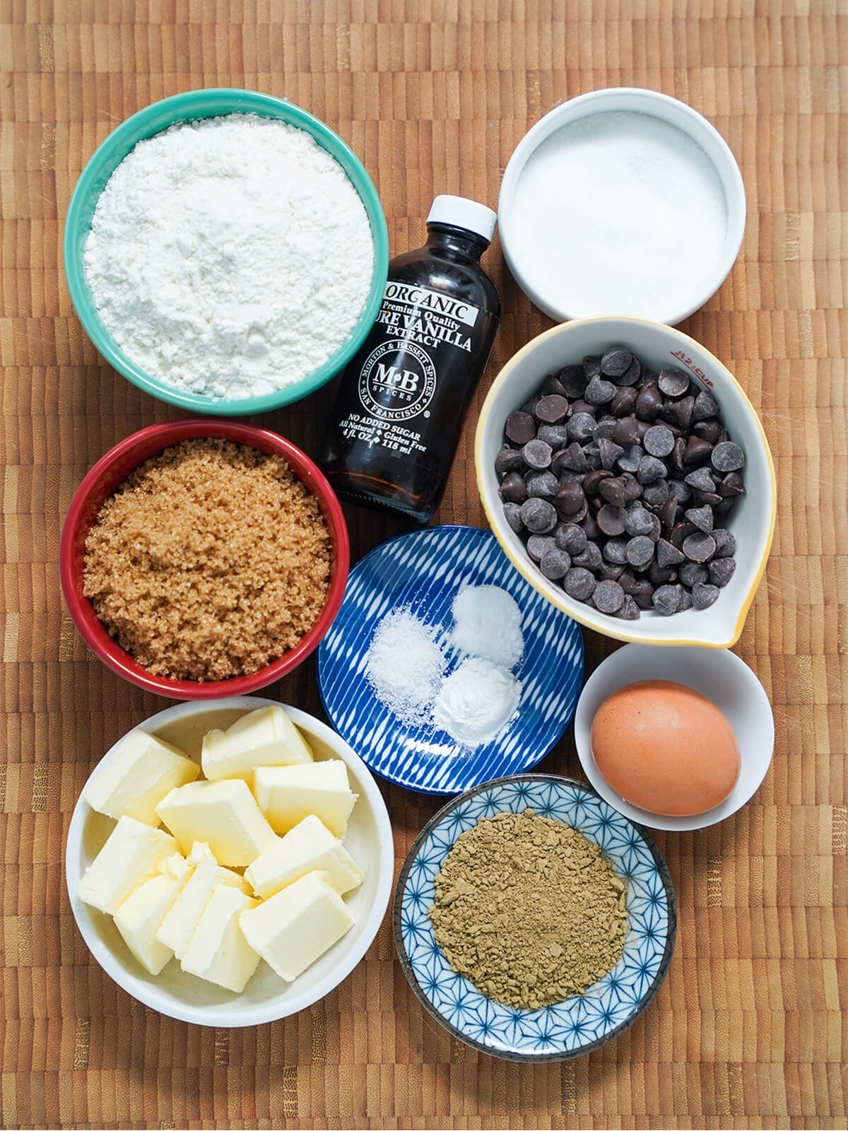 ingredients for hojicha chocolate chip cookies bowls of sugars, flour, chocolate chips, butter, hojicha powder, egg and bottle of vanilla.