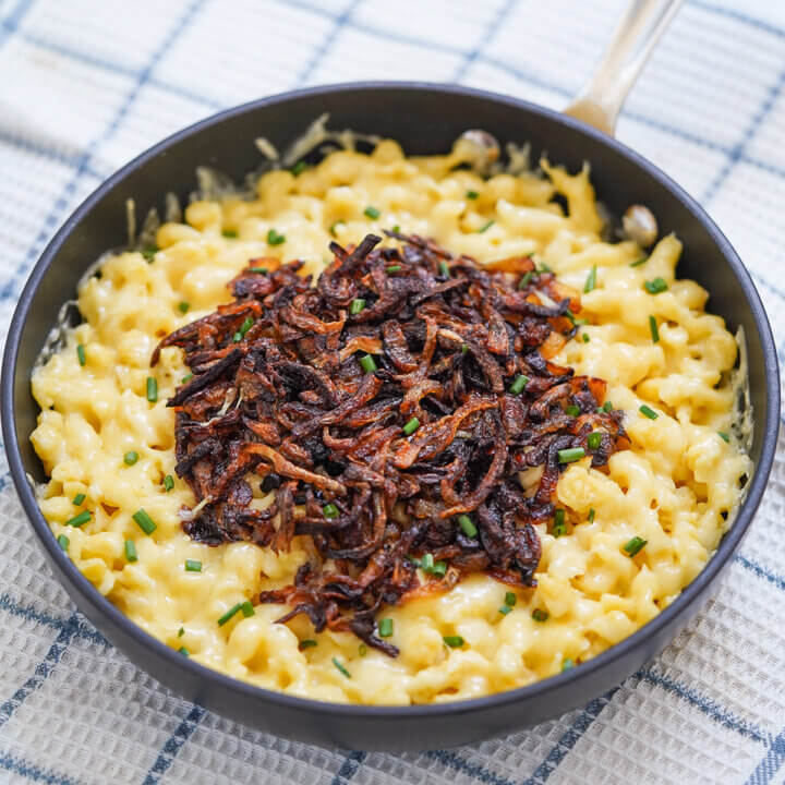 side view of skillet of kaesespaetzle cheese spaetzle topped with onion.