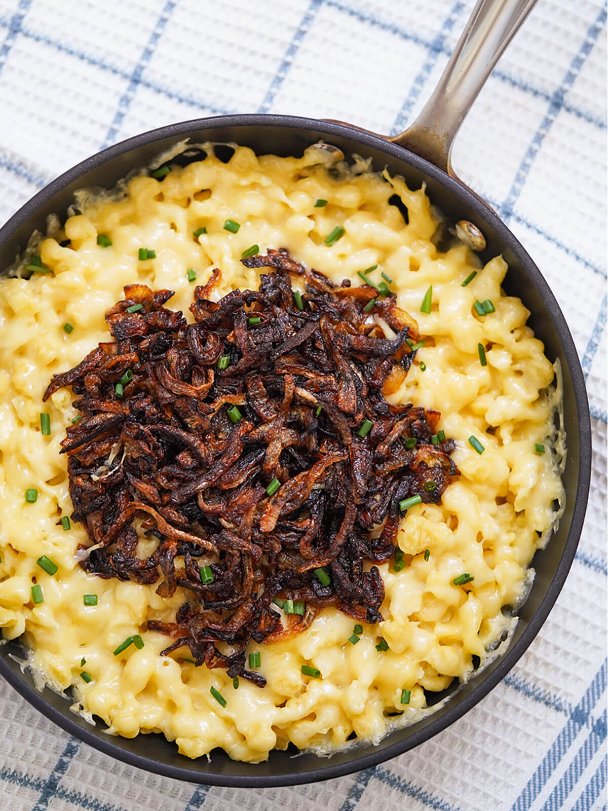 overhead close view of skillet of kaesespaetzle cheese spaetzle topped with caramelized onions.