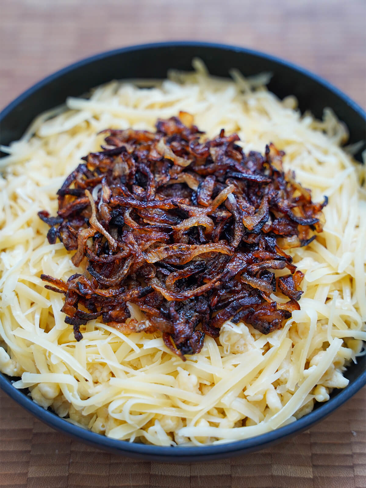 kaesespaetzle before melting cheese in oven. layered spaetzle and cheese, topped with onions, in skillet before melting in the oven.