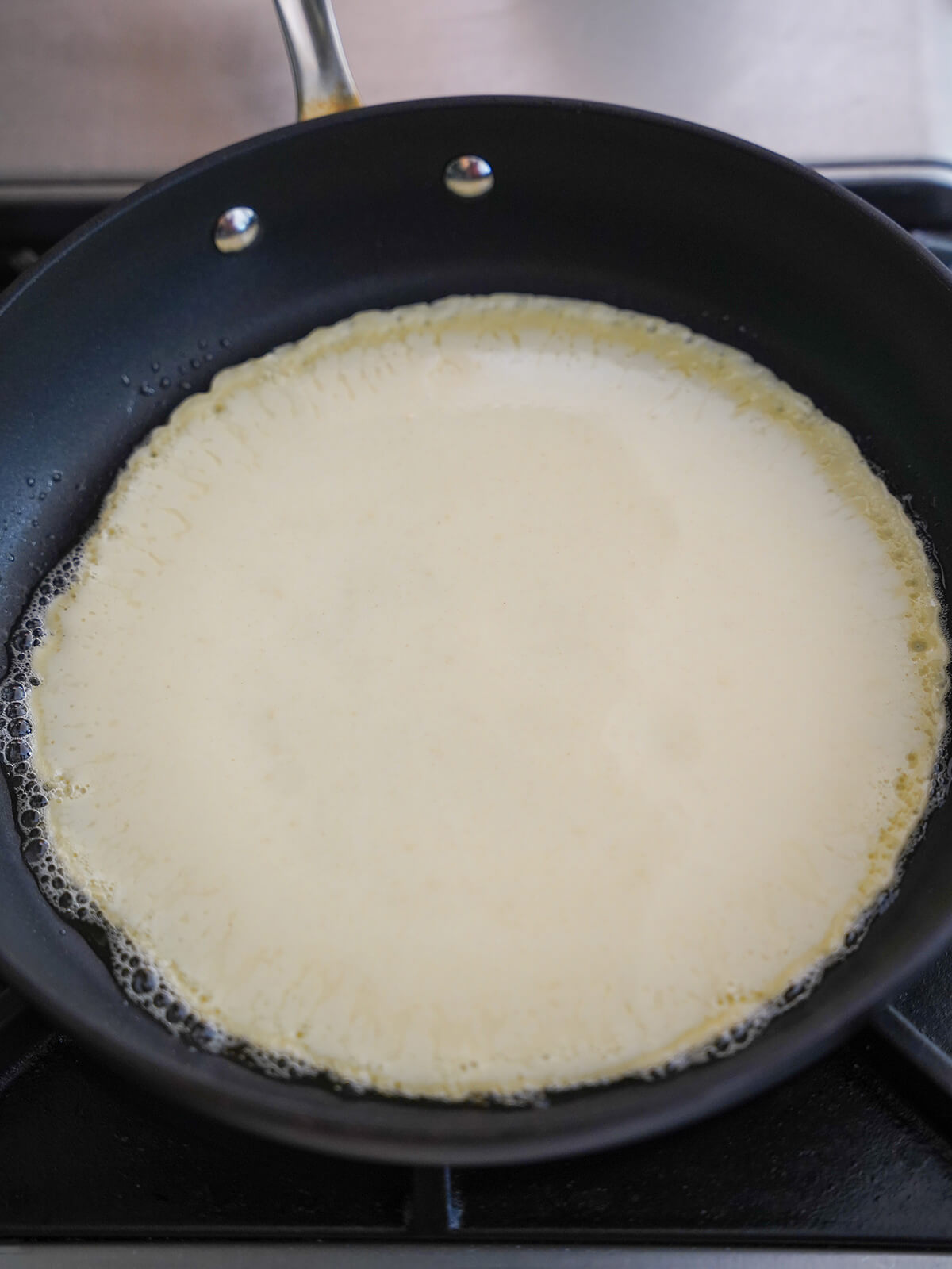 pancake batter in skillet with bubbles of butter around edges.