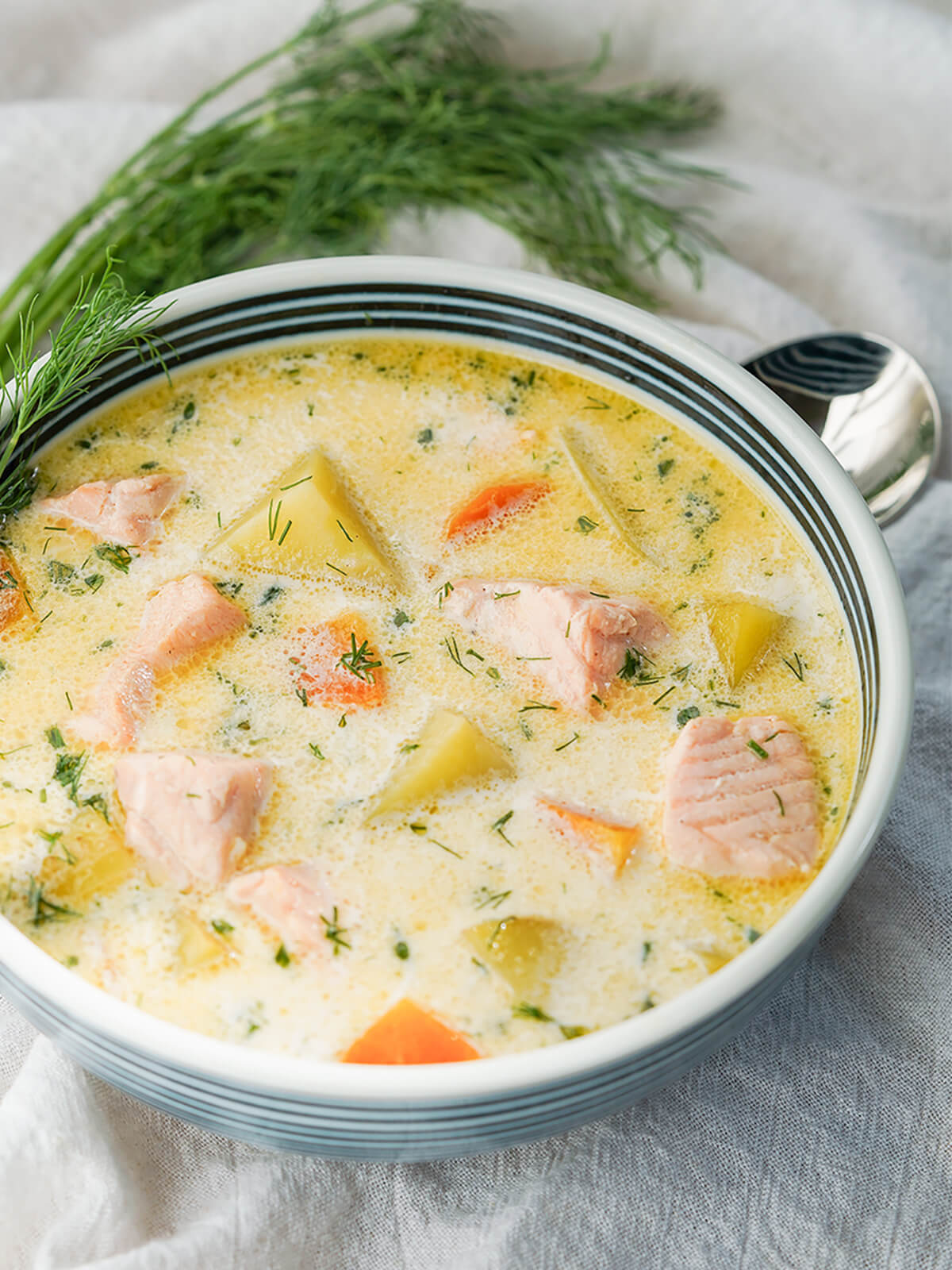 side view of bowl of Finnish salmon soup with bunch of dill and spoon behind bowl.