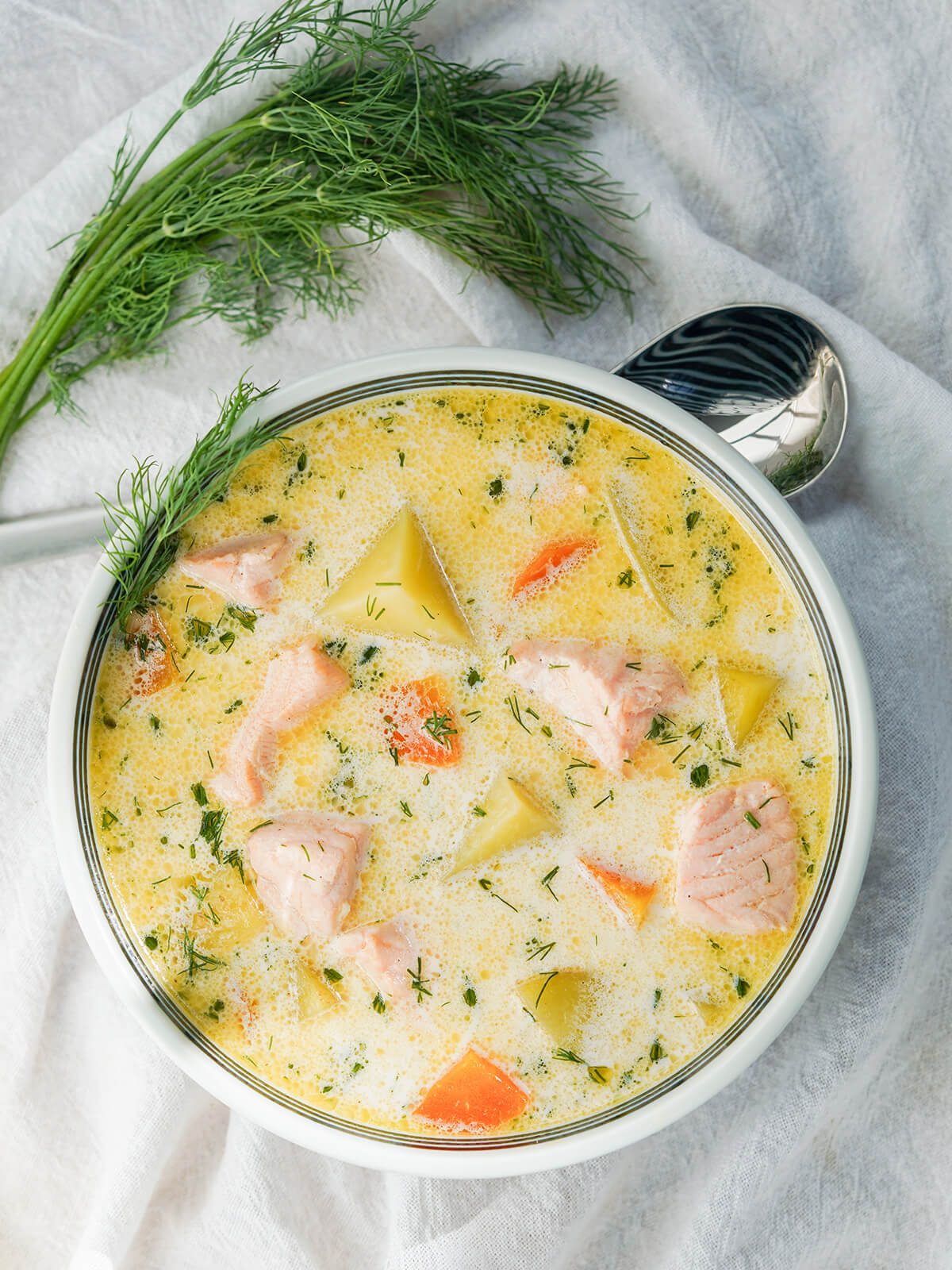 overhead view of bowl of Finnish salmon soup with bunch of dill and spoon above bowl.