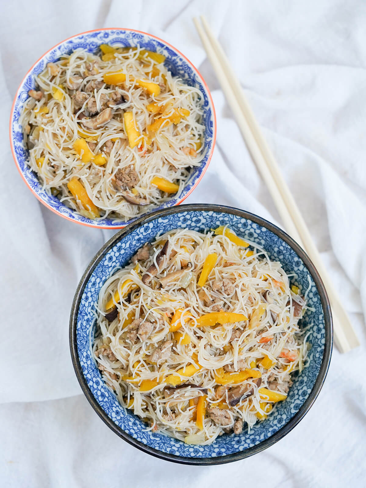 two bowls of Taiwanese pumpkin rice vermicelli noodles overhead view of two bowls of Taiwanese pumpkin rice vermicelli noodles with chopsticks to side.