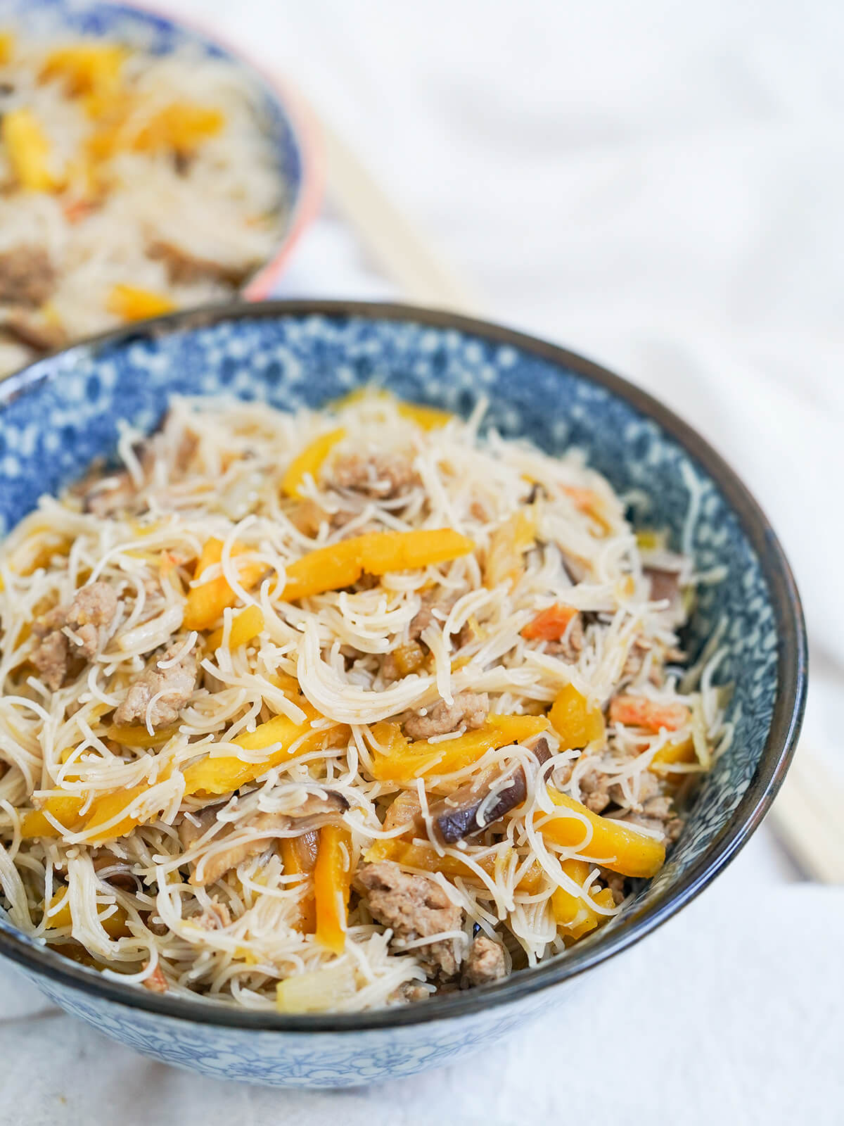 These Taiwanese pumpkin rice vermicelli noodles are a fast and flavorful one pot meal. With a tasty umami flavors, it's filling without being heavy. Perfect for any night. side view of bowl of Taiwanese pumpkin rice vermicelli noodles with second bowl blurred behind.