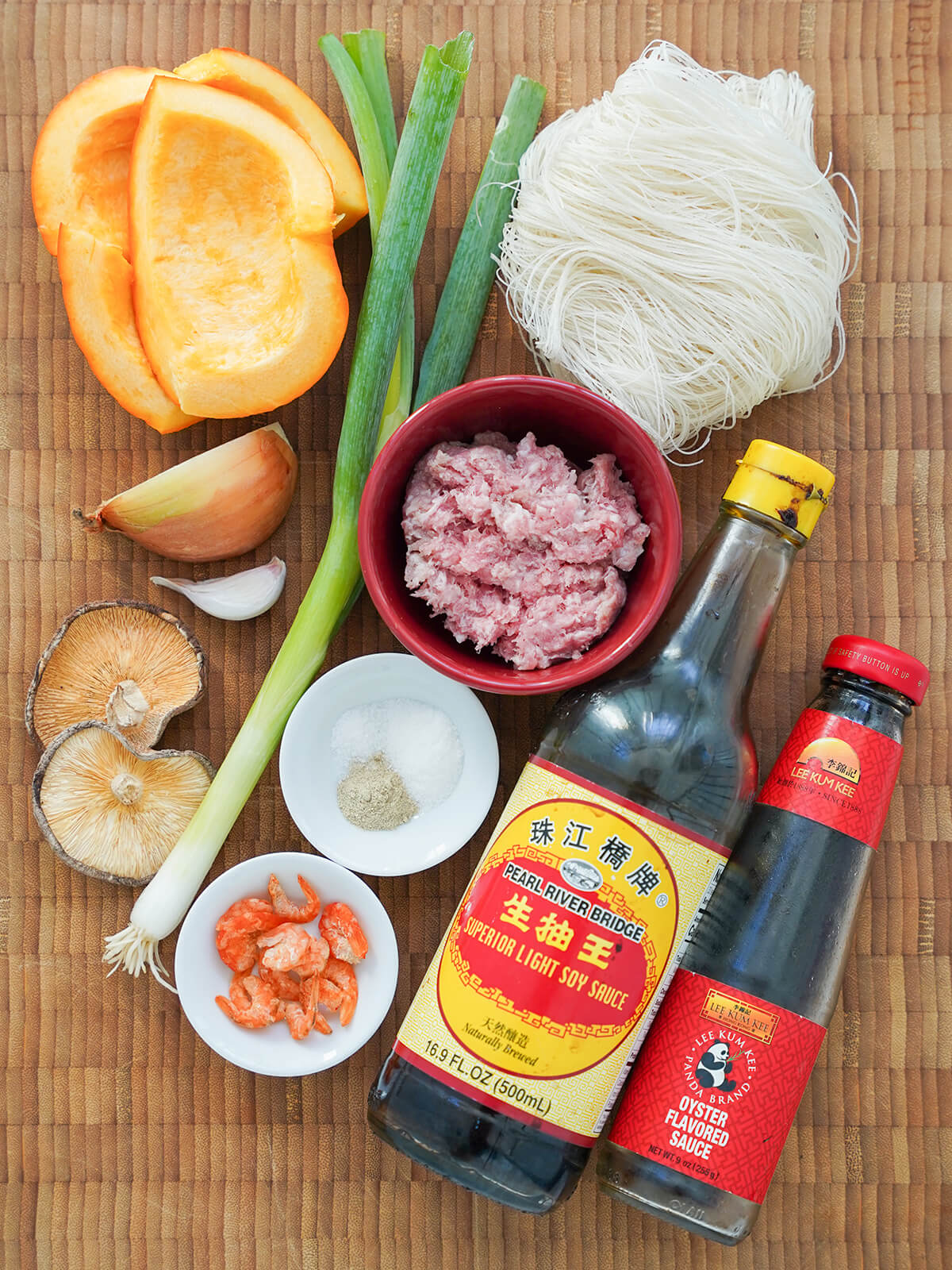 ingredients for Taiwanese pumpkin rice vermicelli noodles pieces of pumpkin, onion, garlic, green onion, deied shitake, dried shrimp, bottles of soy and oyster sauce, dried rice noodles and dish of pork on board.