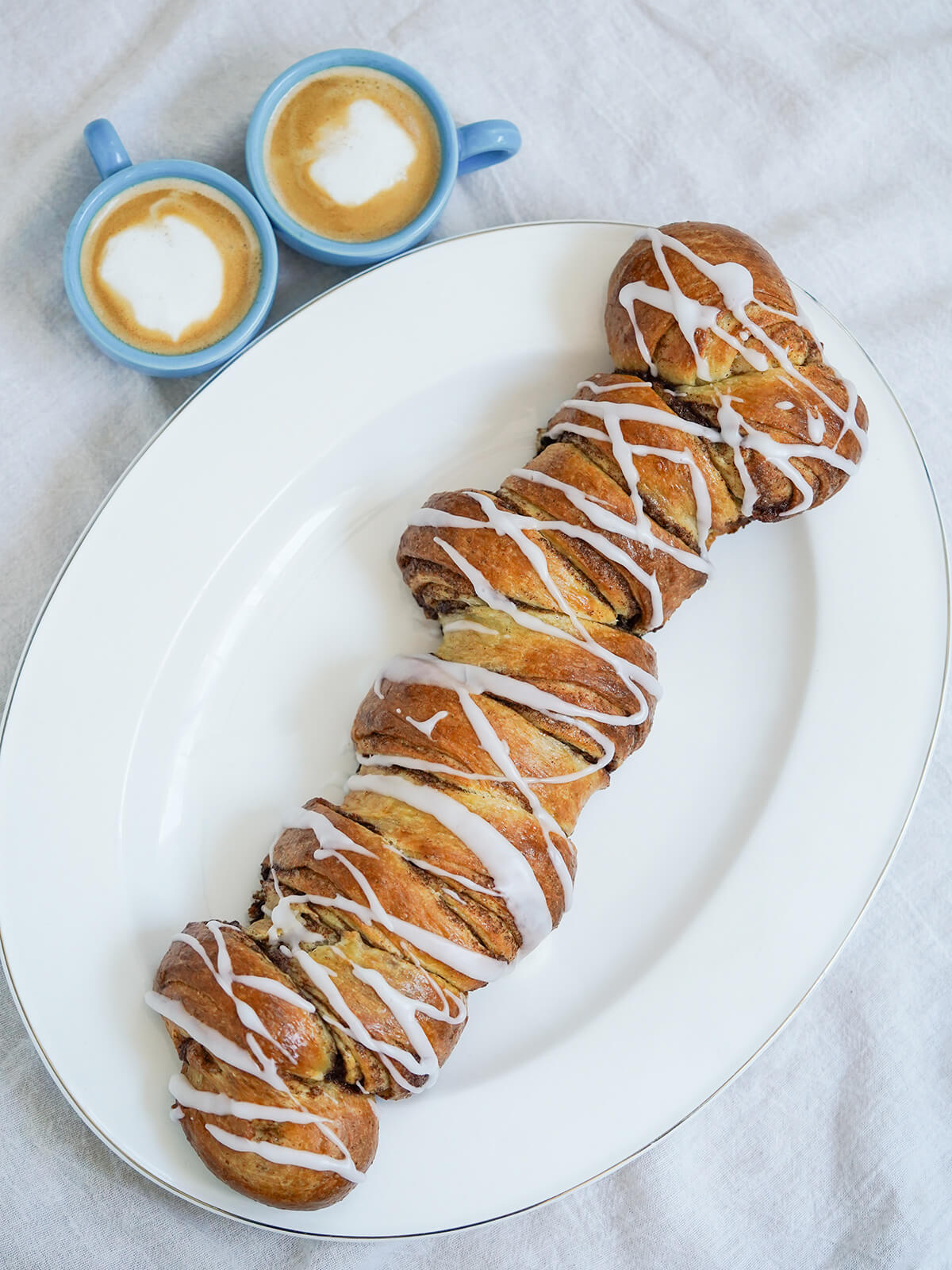 whole kanelstang, Danish cinnamon twist overhead view of whole kanelstang Danish cinnamon twist with two cups of coffee to side of plate.
