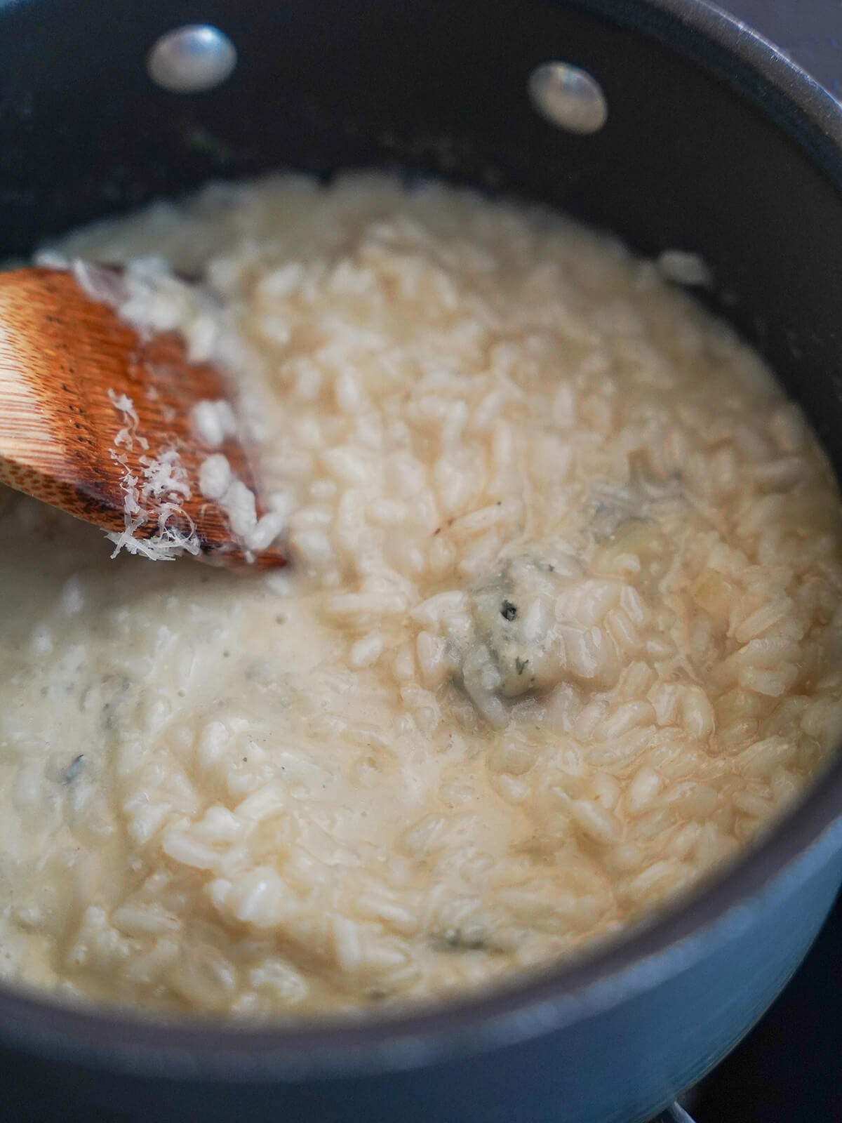 stirring gorgonzola into risotto stirring risotto in pot.